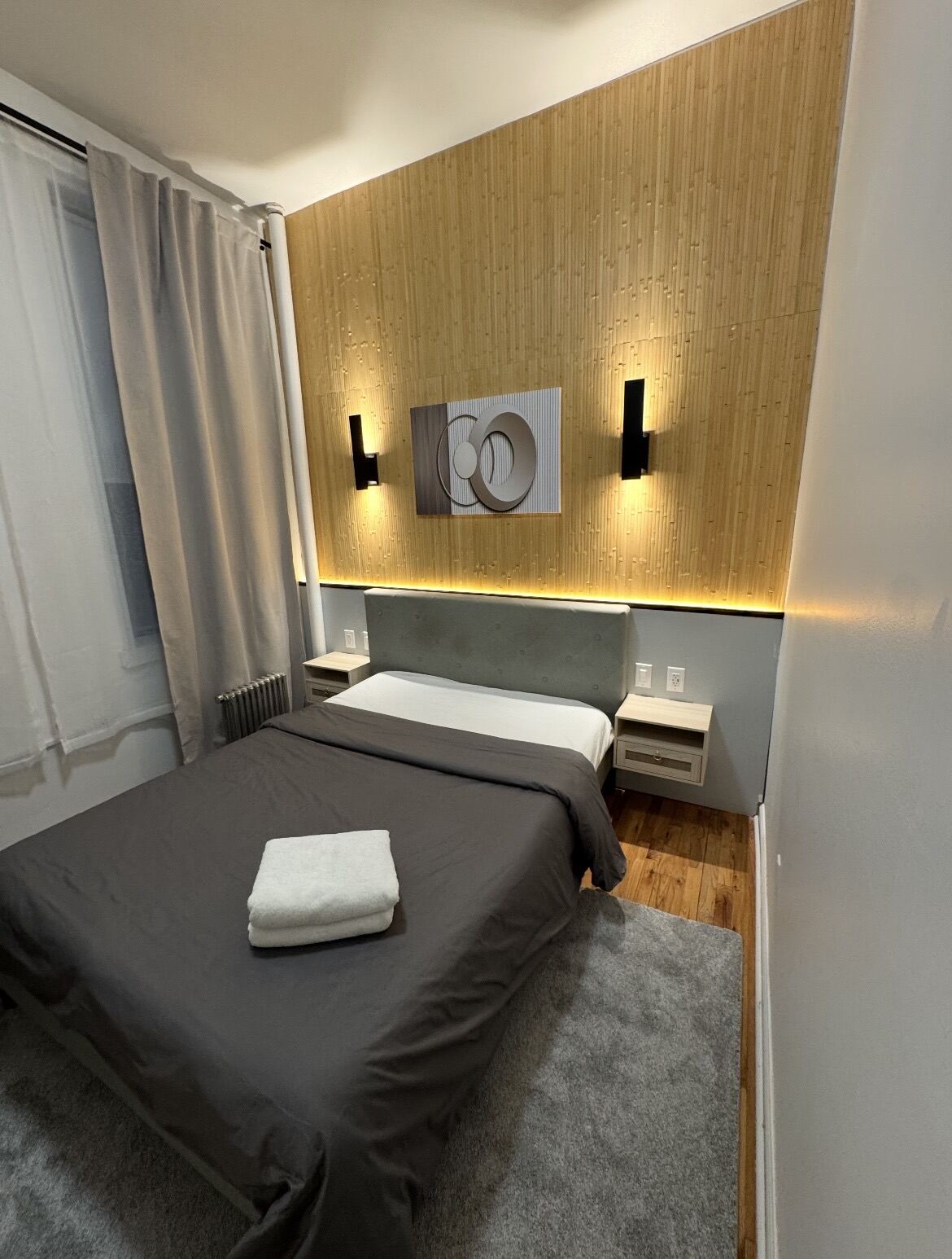 Finished bedroom with a wood accent wall, wall sconces, and a hardwood floor