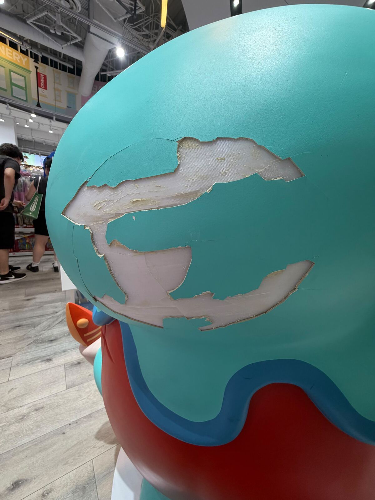 Teal and red fiberglass mascot statue with visible cracks and surface damage