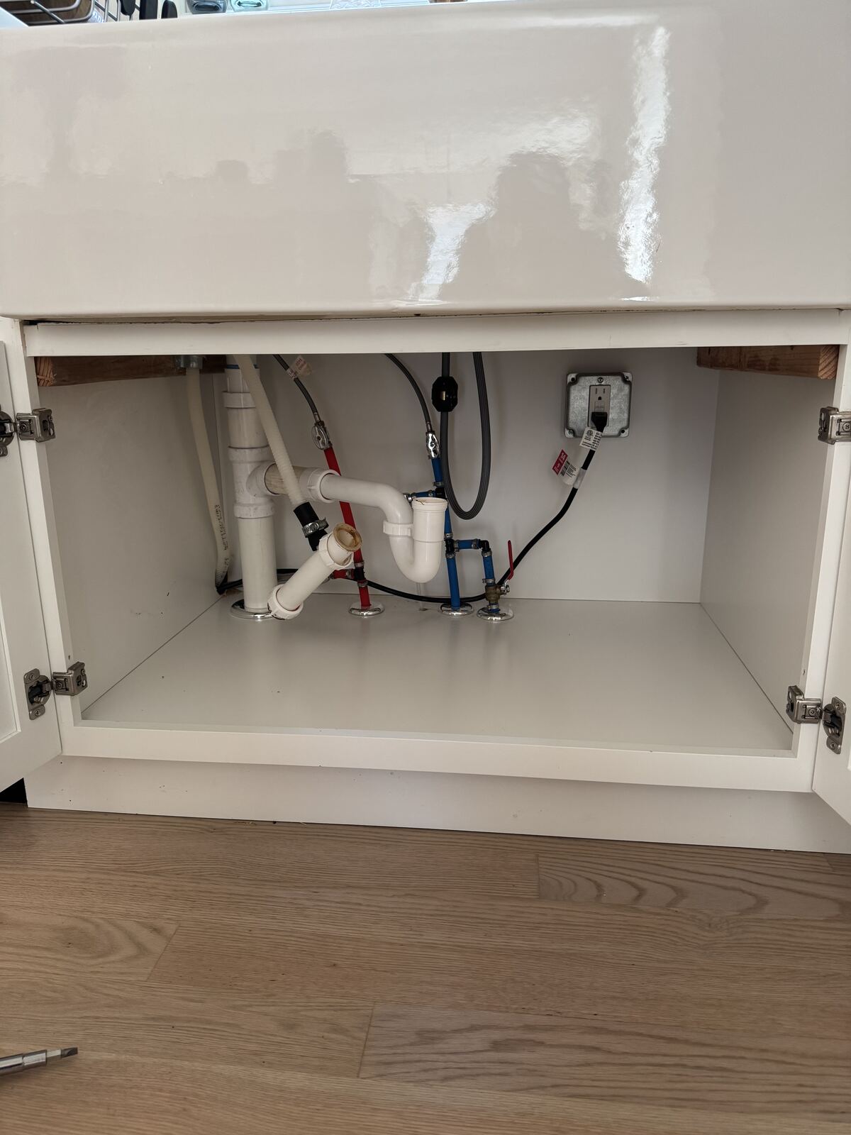 Open cabinet below a sink showing supply lines, drain plumbing, and an electrical outlet